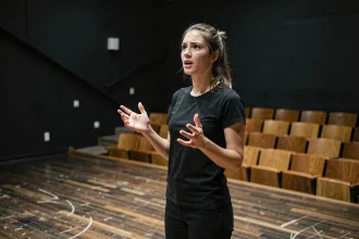 Jeune comédienne en répétition sur scène dans un théâtre de cours d'art dramatique, exprimant une émotion intense dans une salle noire